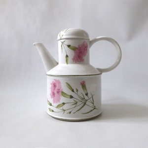 May include: White ceramic teapot with a floral design featuring pink carnations and green leaves. The teapot has a lid and a handle.