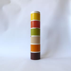 May include: A vertical stack of six cylindrical containers in various colours. The colours include yellow, orange, green, beige, and brown. Each container has a white band and a white lid. The containers are likely for storage.