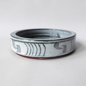 May include: A white ceramic bowl with a blue glaze and a black and white geometric design around the rim.