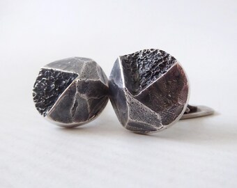 May include: Silver cufflinks with a geometric design. Each cufflink features textured and smooth sections, creating a contrast. The metal has a dark, aged appearance. The cufflinks are a stylish accessory.