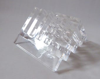 Könnte beinhalten: Ein transparenter Acryl-Displayständer mit einem gestuften, mehrstufigen Design mit vier separaten Schlitzen. Das durchsichtige Material hat eine glatte, polierte Oberfläche und bildet eine strukturierte, kantige Form, die Durchsicht ermöglicht.