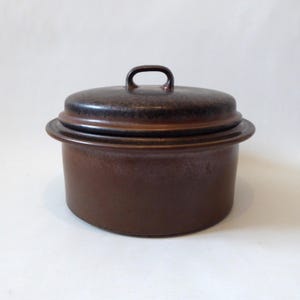 May include: A brown ceramic casserole dish with a lid. The dish has a rounded body and a lid with a small handle. The color is a deep, earthy brown with a slightly textured surface. The dish is designed for cooking and serving.
