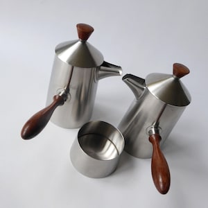 May include: A set of two silver coffee pots with wooden handles and lids. The pots have a modern design and are perfect for serving coffee or tea.