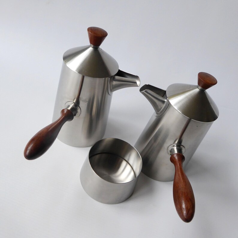 May include: A set of two silver coffee pots with wooden handles and lids. The pots have a modern design and are perfect for serving coffee or tea.