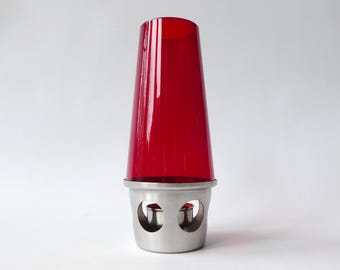 May include: A red glass candle holder with a stainless steel base. The candle holder has a cylindrical shape with a flared top. The base has two circular cutouts. The candle holder is designed to hold a single candle.
