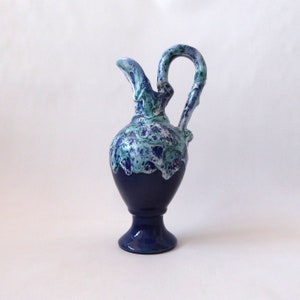 May include: A blue ceramic pitcher with a white and green glaze. The pitcher has a unique, wavy design and a wide base.