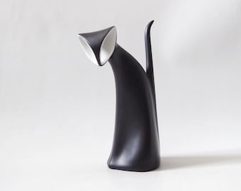 Könnte beinhalten: Eine mattschwarze Katzenfigur mit einem glatten, länglichen Körper und einem hohen, aufrechten Schwanz. Der Kopf der Katze ist nach unten geneigt und gibt den Blick auf eine kontrastierende weiße Innenfläche an Ohren und Gesicht frei.