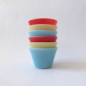 May include: A stack of five vintage glass cups in various colours, including red, yellow, and blue. The cups are stacked in a pyramid shape, with the largest cup at the bottom and the smallest cup at the top.