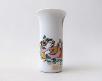 Könnte beinhalten: Eine weiße Porzellanvase mit einer farbenfrohen Illustration einer Person, die ein lautenartiges Saiteninstrument spielt. Das Design enthält lebendige Akzente in Pink, Gelb, Blau und Grün, mit einem ausgestellten Rand und einer zylindrischen Form.
