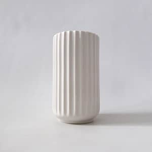 May include: A white ceramic vase with a ribbed, vertical design. The vase has a cylindrical shape with a slightly rounded base and a textured, fluted surface. The top edge has a subtle, scalloped detail.