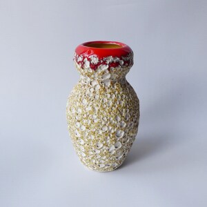 May include: A white ceramic vase with a textured surface and a red rim. The vase has a rounded shape and a wide opening.