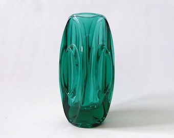 Könnte beinhalten: Eine hohe, zylindrische Vase aus smaragdgrünem Glas mit einer Reihe vertikaler, ovaler Vertiefungen an der Außenseite. Das Glas ist durchscheinend, lässt Licht hindurch und die Oberfläche ist glatt mit einem polierten Finish.