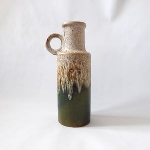 May include: A tall ceramic vase with a single circular handle near the top. The upper portion features a speckled beige and cream glaze, while the lower section transitions into a solid dark olive green with a vertical drip pattern effect.