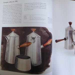 May include: A set of three silver coffee pots with wooden handles. The pots are designed in a contemporary style with a rounded shape and a spout on the side. The pots are sitting on a dark brown surface.