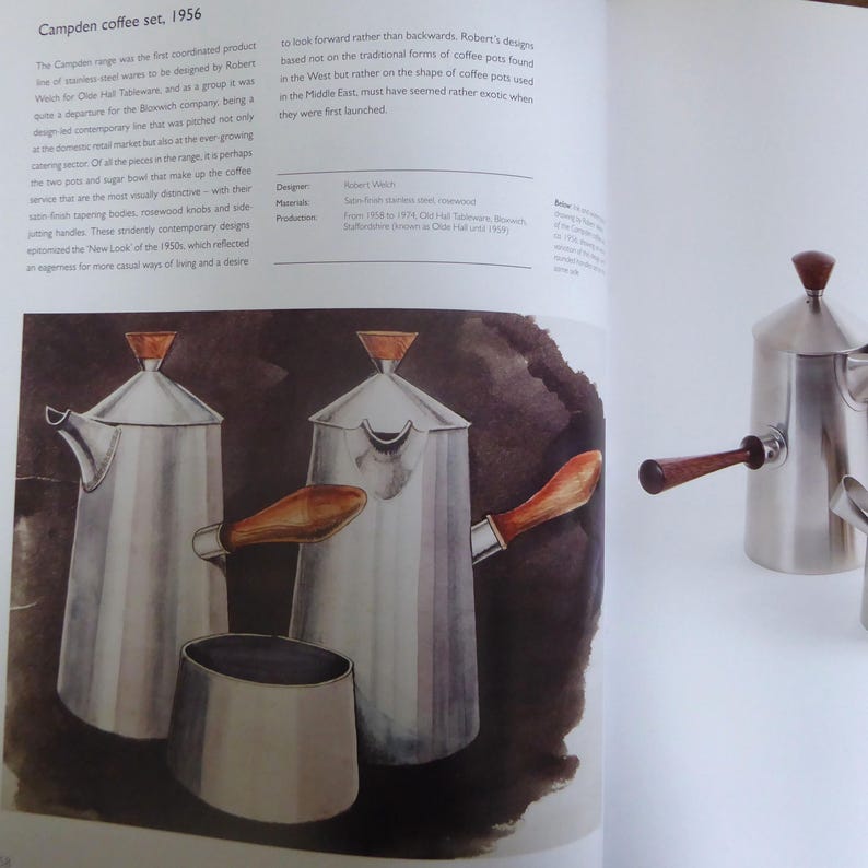 May include: A set of three silver coffee pots with wooden handles. The pots are designed in a contemporary style with a rounded shape and a spout on the side. The pots are sitting on a dark brown surface.