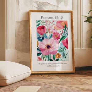 May include: A framed print with a floral design in shades of pink, red, and green. The print features the text "Romans 12:12" and the quote "Be joyful in hope, patient in affliction, faithful in prayer."
