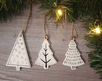 May include: Three white ceramic Christmas tree ornaments with different designs. One has gold dots, one has a black tree branch, and one has a black and white striped pattern.