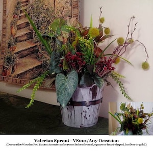 May include: A faux plant arrangement in a rustic wooden pot with a metal band. The arrangement features green leaves, red berries, and small yellow flower buds. The pot has a distressed white finish and a silver button accent.