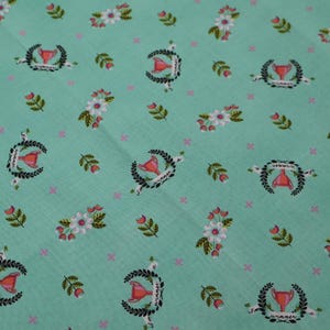 May include: A light teal fabric with a repeating pattern of floral bouquets, laurel wreaths, and trophy-like shapes. The design includes white flowers with pink centers, green leaves, and small pink crosses. The fabric has a subtle textured appearance.
