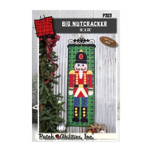 May include: A sewing pattern titled Big Nutcracker by Patch Abilities, Inc. featuring a 12 inch by 33 inch wall hanging design. The pattern displays a nutcracker figure on a green plaid background with a black hat, red jacket, and blue pants.