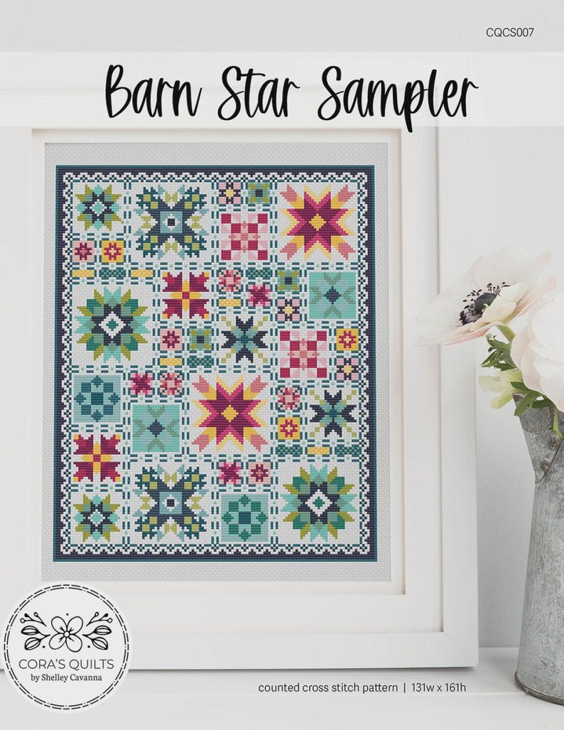 Op de afbeelding: Een ingelijste kruissteek sampler met de titel "Barn Star Sampler". Het ontwerp toont een raster van kleurrijke sterren en geometrische patronen in tinten van teal, roze, geel en rood. Het kunstwerk is ingelijst in een witte lijst en bevat de tekst "CORA'S QUILTS by Shelley Cavanna".