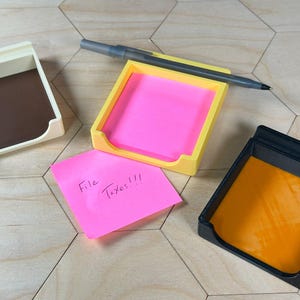 May include: Three desk organizers, one yellow, one white, and one black, with a pink sticky note that says "File Taxes!!!" in black ink.