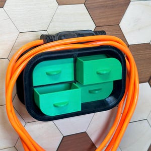 May include: A black and green wall-mounted organizer with four small drawers. The organizer is holding a bright orange electrical cord.