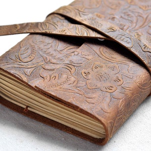 May include: A brown leather journal with a floral embossed design and a leather strap closure.