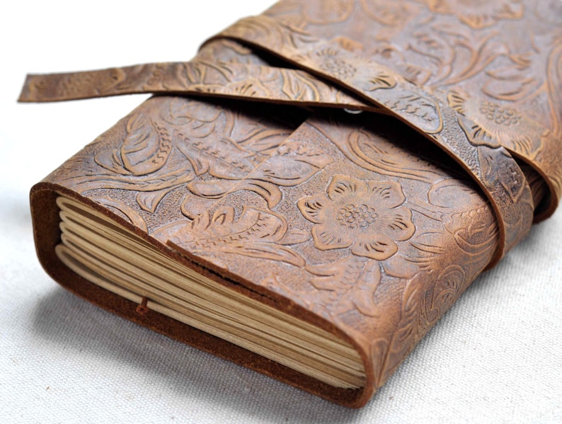 May include: A brown leather journal with a floral embossed design and a leather strap closure.