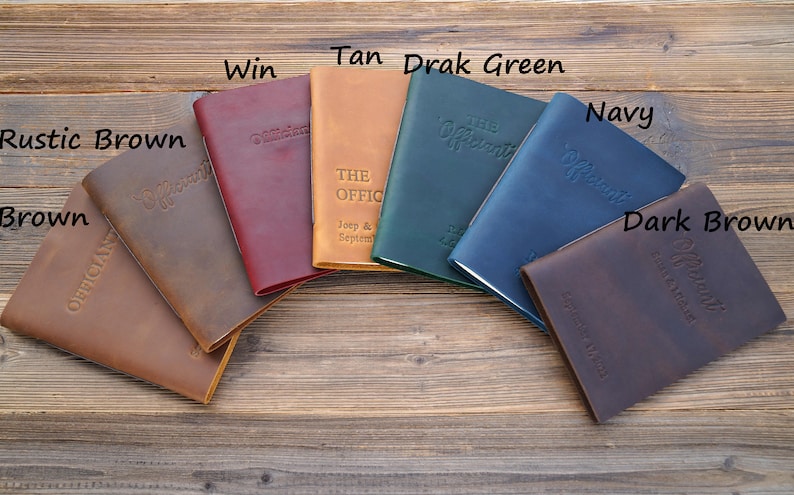May include: Seven leather-bound journals in different colors, including brown, tan, dark brown, navy, green, and burgundy. Each journal has the word "Officiant" embossed on the cover.