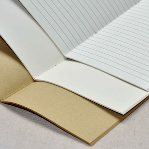 Pu&ograve; includere: Un quaderno marrone con pagine a righe. Il quaderno &egrave; aperto e piegato a met&agrave;, rivelando le pagine bianche all'interno.