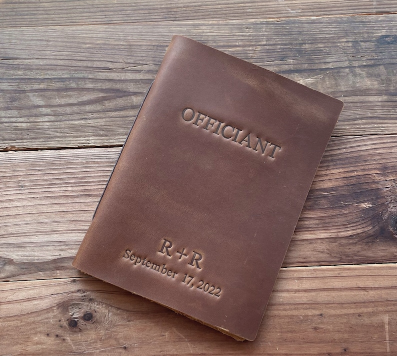 May include: Brown leather-bound book with the word "Officiant" embossed on the front cover. The book also has the text "R+R September 17, 2022" embossed on the front cover.