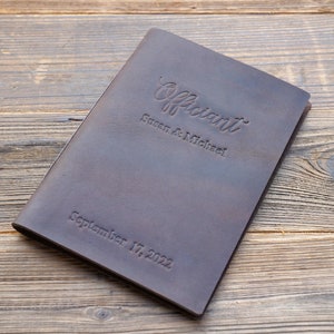 May include: A brown leather-bound journal with the word "Officiant" embossed on the front cover. The names "Susan & Michael" and the date "September 17, 2022" are also embossed on the cover.