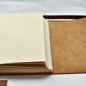 May include: A brown leather-bound journal with blank pages and a strap closure. The journal is open to reveal the blank pages.