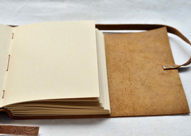 May include: A brown leather-bound journal with blank pages and a strap closure. The journal is open to reveal the blank pages.