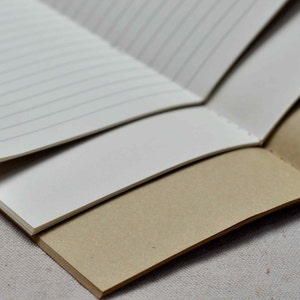 May include: A brown notebook with lined paper and a cream-colored cover. The notebook is open and folded in half, revealing the lined pages.