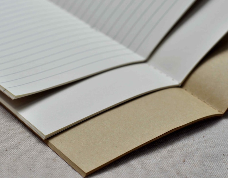 May include: A brown notebook with lined paper and a cream-colored cover. The notebook is open and folded in half, revealing the lined pages.