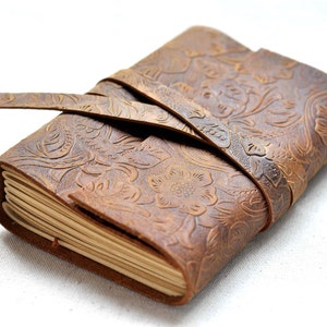 May include: A brown leather journal with a floral embossed design and a leather strap closure.