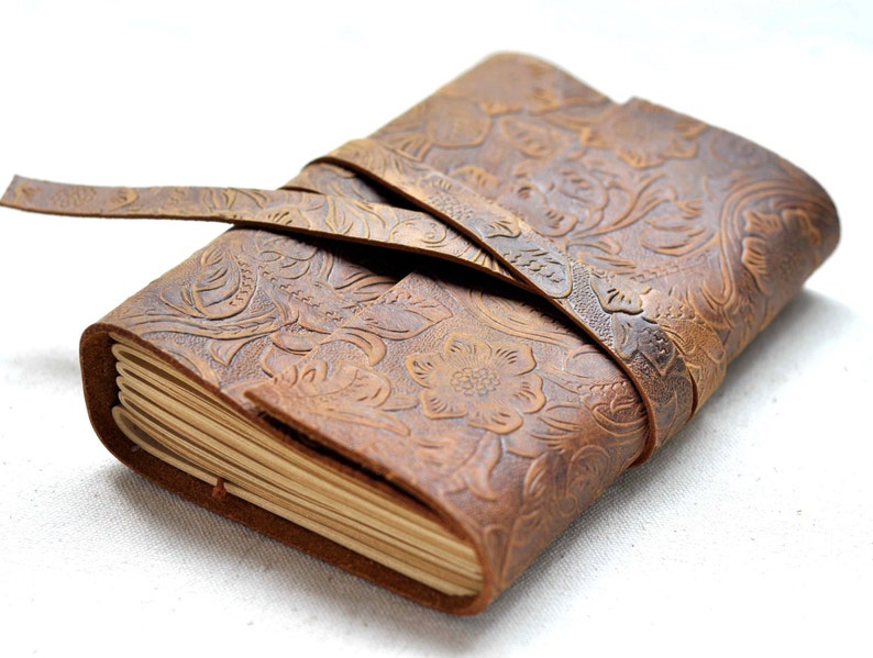 May include: A brown leather journal with a floral embossed design and a leather strap closure.