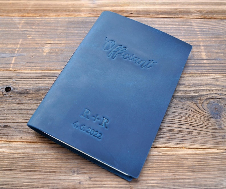 May include: A dark blue leather-bound journal with the word "Officiant" embossed on the front cover. The journal also has the initials "R+R" and the date "4.6.2022" embossed on the front cover.