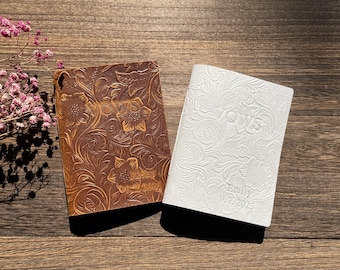 May include: Two leather journals with floral embossed designs. One is brown, the other is white. The brown journal has the word "Yours" embossed on it. The white journal has the name "Emily" and the date "9.7.2025" embossed on it.