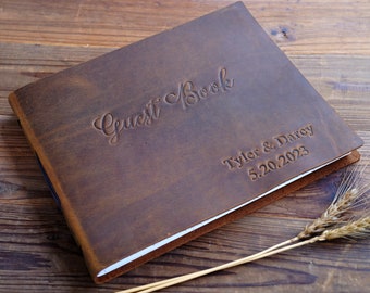 Puede incluir: Un libro de visitas de cuero marrón con las palabras "Guest Book" y "Tyler & Darcy 5.20.2023" grabadas en la portada.
