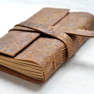 May include: A brown leather journal with a floral embossed design and a leather strap closure.