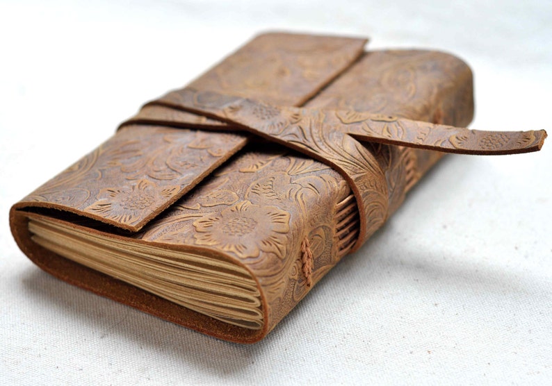 May include: A brown leather journal with a floral embossed design and a leather strap closure.