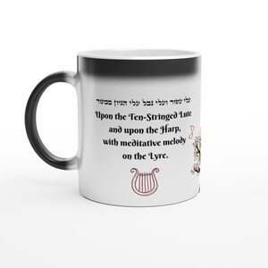 Puede incluir: Una taza de cerámica blanca con un asa negra. La taza presenta texto en inglés y hebreo, junto con un dibujo de una lira. El texto dice "Upon the Ten-Stringed Lute and upon the Harp, with meditative melody on the Lyre."