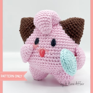 May include: Pink crocheted amigurumi toy with brown ears and a blue lollipop. The toy has black eyes and a pink tongue sticking out. The text "PATTERN ONLY" is visible in the lower left corner of the image. The text "by A Hare Affair" is visible in the lower right corner of the image.