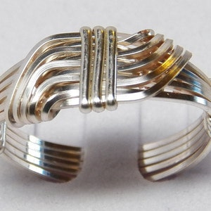 May include: A silver wire ring with a woven design. The ring is made of multiple strands of wire that are woven together to create a unique and intricate pattern.