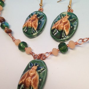 May include: A green and brown ceramic bee pendant necklace with matching earrings. The necklace features copper wire and green and beige beads.