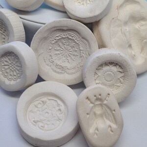 May include: A collection of white ceramic molds with various intricate designs, including floral patterns, geometric shapes, and a stylized insect. The molds are ideal for creating decorative cookies, fondant, or other edible treats.