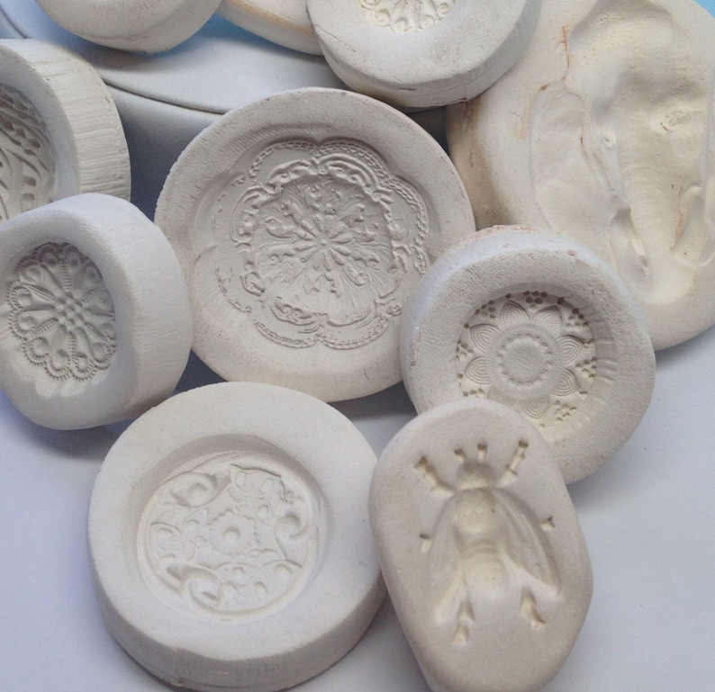 May include: A collection of white ceramic molds with various intricate designs, including floral patterns, geometric shapes, and a stylized insect. The molds are ideal for creating decorative cookies, fondant, or other edible treats.